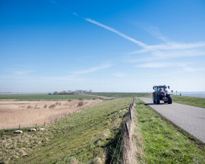 tractor on dyke in countryside landscape under blue sky in dutch province of zeeland