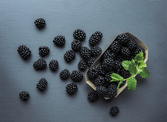 Top view on box with blackberries and several other pieces laying on grey textured table.