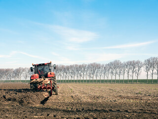 Obraz premium tractor with plough on field early spring in the netherlands on the island of goeree en overflakkee