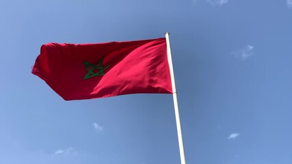 Moroccan red flag waving around outdoors with a blue sky in the background