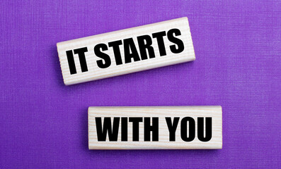 On a lilac bright background, light wooden blocks with the text IT STARTS WITH YOU