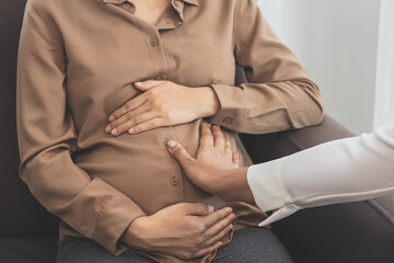 Young asian pregnant woman holding her belly while gynecologist check up the symptoms by touching  her abdomen about the pregnancy is explaining about the unborn child.
