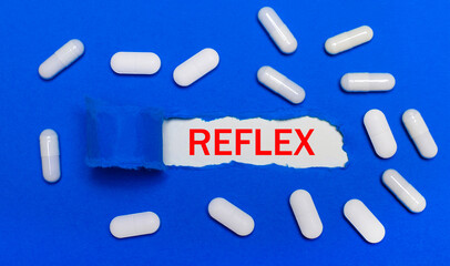 White pills lie on a beautiful blue background. In the center is white paper with the inscription REFLEX. Medical concept. View from above.