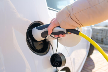 Close up woman hand inserts power cable supply to charge electric or EV car.