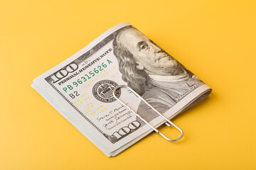 The 100 dollar bills are folded in half and held together with a paper clip on yellow background. Closeup view.