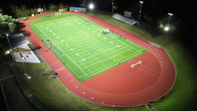 Cinematic aerial drone footage high school team practicing American football on an illuminated athletic sports field at night at Bellevue High School, in Washington State
