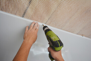 A builder is installing plastic ceiling panel, white PVC bathroom ceiling cladding in a bathroom...