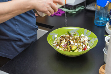 Close up view of a woman adding salt to a salad bowl. Healthy food concept. 