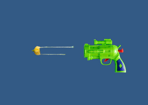 green plastic gun toy with flower  yellow bullets in the air on blue background. summer background.