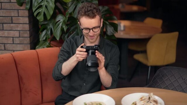 Handsome young man takes pictures of dishes in a cafe