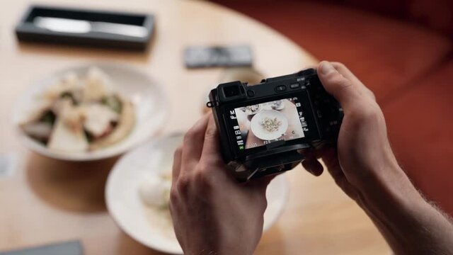 Close-up of male hands holding a mirrorless camera and taking pictures of food on the table