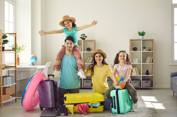 Portrait of cheerful young parents and their two daughters sitting on the floor and packing...