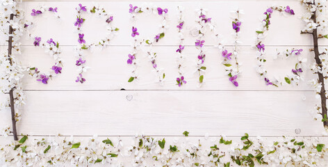 Composition of spring flowers, blooming tree branches on a white wooden background. Lettering Spring made of white and purple flowers and leaves. Flat lay, top view, close up, copy space