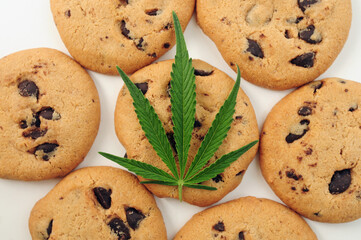 Sweets with CBD oil. Marijuana leaf on white background. Cannabis oil and chocolate cookies close-up. Top view, flat lay.