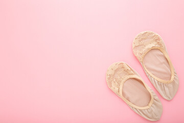 Female brown nylon lace foot slips on light pink table background. Pastel color. Closeup. Empty place for text. Top down view.