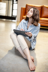 Woman works on a digital tablet while sitting on the floor