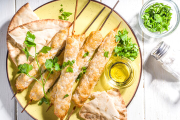 Chicken shish kebabs on wooden skewers sticks top view. Traditional Mediterranean dish kebaps with ground chicken meat, sunny white wooden background copy space