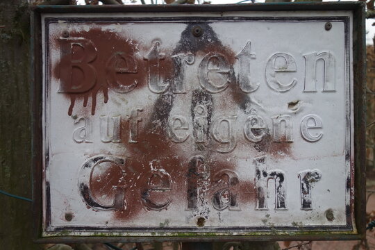 Marodiertes, mit Graffiti bemaltes  Warnschild: Betreten auf eigene Gefahr! Typisch deutsches Schild unleserlich schlecht kaum lesbar.