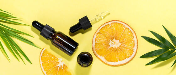 Organic skin care cosmetic products  with vitamin C in glass bottles with dropper on yellow background with palm leaves and orange slices.