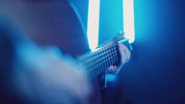 Musician playing acoustic dreadnought guitar with atmospheric coloured lighting
