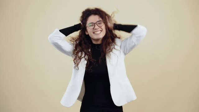 Victorious young woman with curly hair, shakes her hair with her hands and her mouth is watery. Young hipster in gray jacket and white shirt,