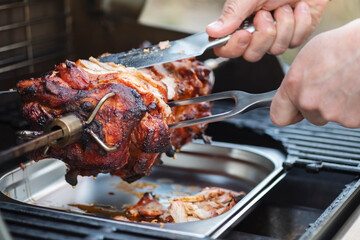 The chef cuts chunks of meat from the spit. Food cooked on a gas grill