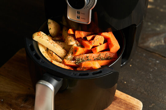 Cooking potatoes and carrot sticks with spices in an air fryer