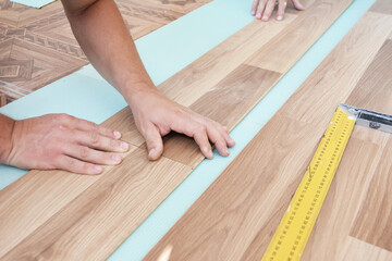 Wood laminate flooring installation: Laminate flooring installers are installing laminate hardwood planks over a soundproofing underlayment, insulation.