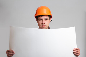 Young fatigue and angry construction worker in hard hat holding paper project on grey studio background