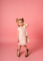 a little girl in a lace dress and shoes on a pink background with a place for text