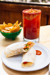 Mexican burrito and michelada beer with tomato juice with copy space. Michelada beer with tomato juice and burritos. Mexican food on wooden table. Concept of traditional food and mexican drink.