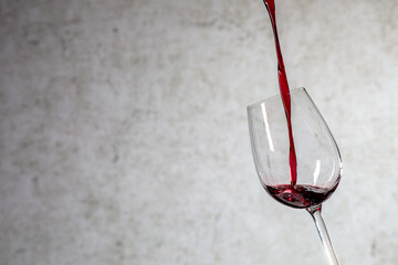 Gießen von Rotwein aus der Flasche in ein Glas auf verschwommenen hellen Hintergrund, Nahaufnahme....
