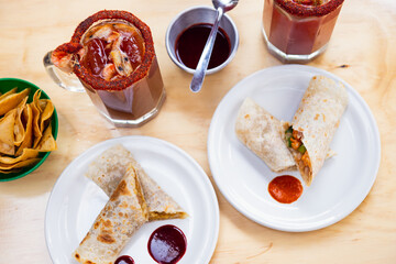 Mexican burrito and michelada beer with tomato juice with copy space. Michelada beer with tomato juice and burritos. Mexican food on wooden table. Concept of traditional food and mexican drink.