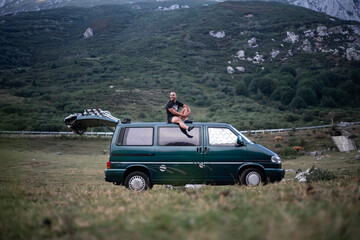 Fototapeta premium Young man sitting on the roof of his green camper van