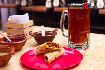 Mexican burrito and michelada beer with tomato juice with copy space. Michelada beer with tomato juice and burritos. Mexican food on wooden table. Concept of traditional food and mexican drink.