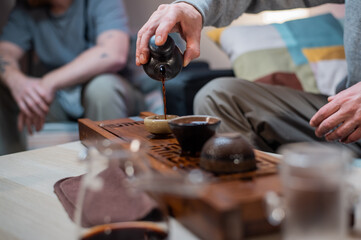 Two friends pour tea into special clay cups to drink a delicious drink in a cozy home atmosphere. Close-up with a blurry background.
