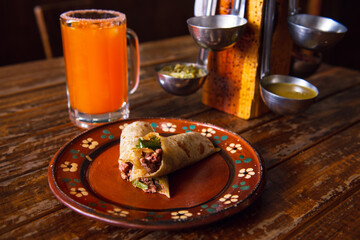 Mexican burrito and michelada beer with tomato juice with copy space. Michelada beer with tomato juice and burritos. Mexican food on wooden table. Concept of traditional food and mexican drink.