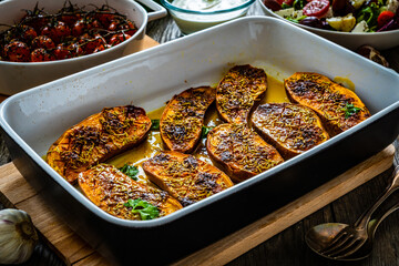 Roasted sweet potatoes  in cooking pan and vegetables on wooden table
