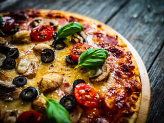 Pizza with white mushrooms, ham, tomatoes, olives, parmesan and mozzarella on wooden background
