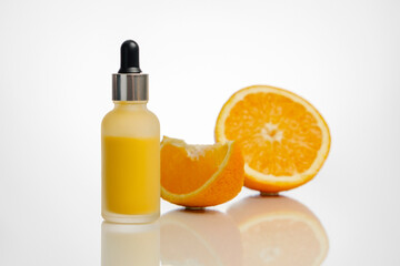 A bottle of orange serum and some oranges in the background.