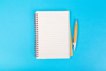 stack of school exercise books on blue background, spiral notepad with blank page and pen on table...