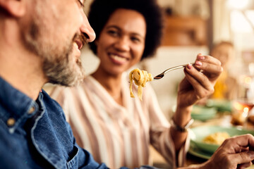 Close-up of black woman feeding her Caucasian husband during lunch at dining table.