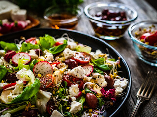 Fresh vegetable salad - feta cheese, tomatoes, radish, artichokes , lettuce, black olives and sprouts on wooden table
