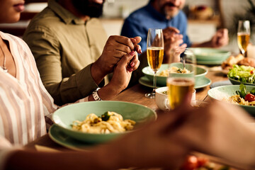 Close-up of friends holding hands and saying grace at dining table.
