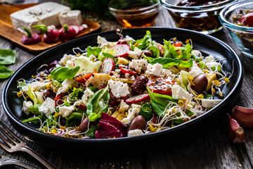 Fresh vegetable salad - feta cheese, tomatoes, radish, artichokes , lettuce, black olives and sprouts on wooden table

