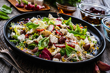 Fresh vegetable salad - feta cheese, tomatoes, radish, artichokes , lettuce, black olives and sprouts on wooden table
