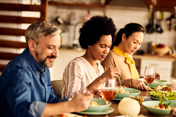 African American woman eating pasta while having lunch with friends at dining table.