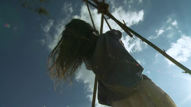 View from below of a young hippie girl standing on a mountain swing in the surroundings of Katmandu, Nepal, hanging from a bamboo pole DIY structure.