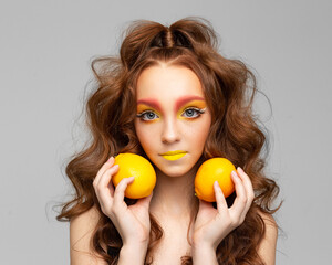 Young girl holding tangerines in her hands with curly and red hair, face with freckles. Yellow lips, citrus fruit.