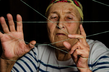 Grandma unravels the threads. Old grandmother close up. The woman is trying to get out of the nets. Manipulation. Infringement of rights. Restriction of human freedom. Isolated person. Delusion - obrazy, fototapety, plakaty